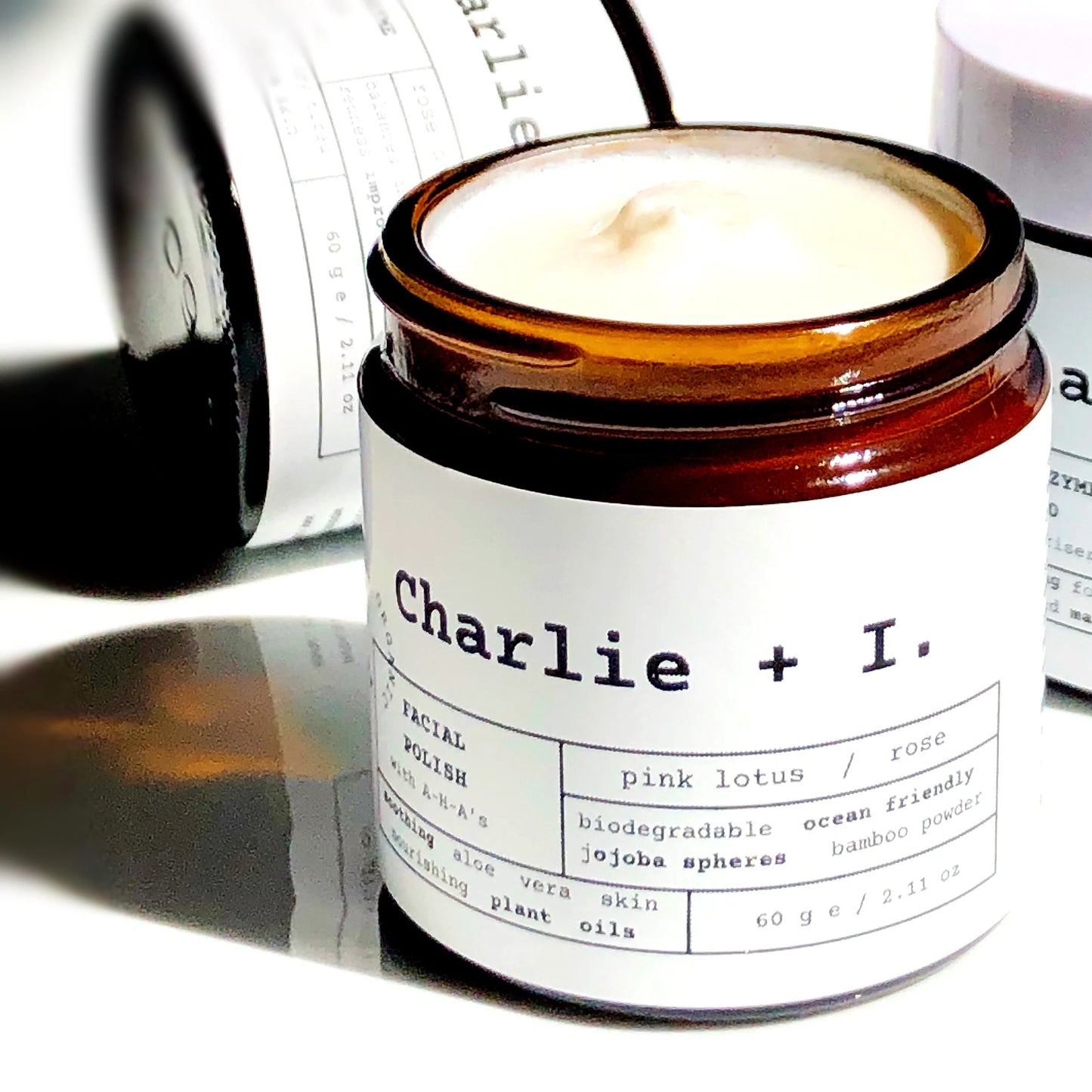 A jar of Pink Lotus + Rose Facial Polish with the label Charlie + I. on it, placed on a surface with a shadow falling over part of the image.