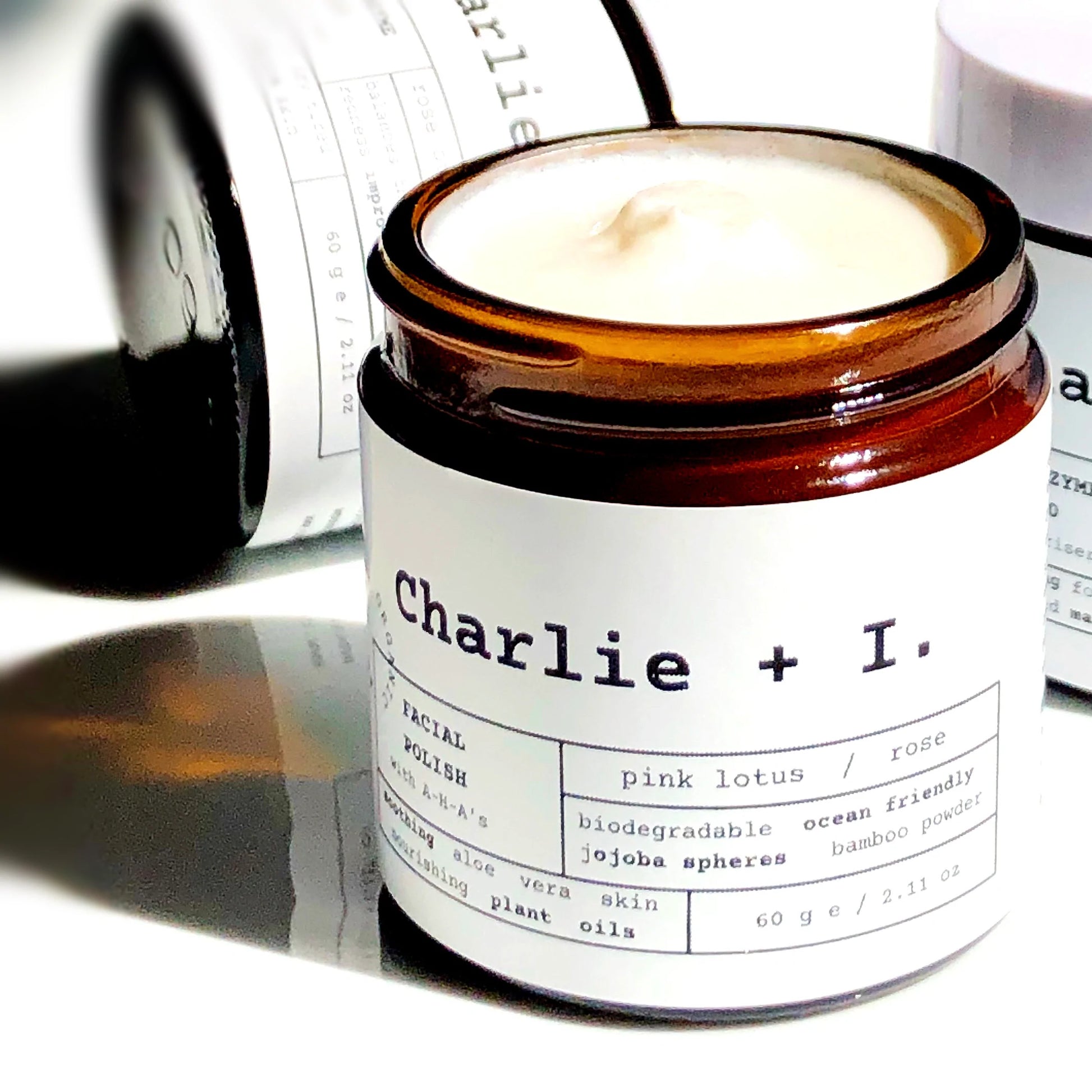 A jar of Pink Lotus + Rose Facial Polish with the label Charlie + I. on it, placed on a surface with a shadow falling over part of the image.